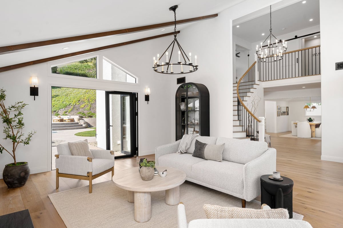 A modern living room with white furniture, wooden floor, and large windows