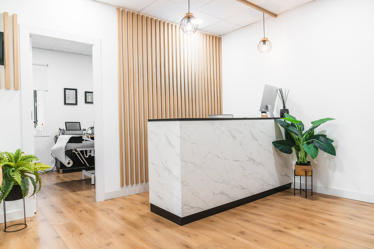 Clean physiotherapy clinic reception area featuring a marble counter, wood panel wall, and plants