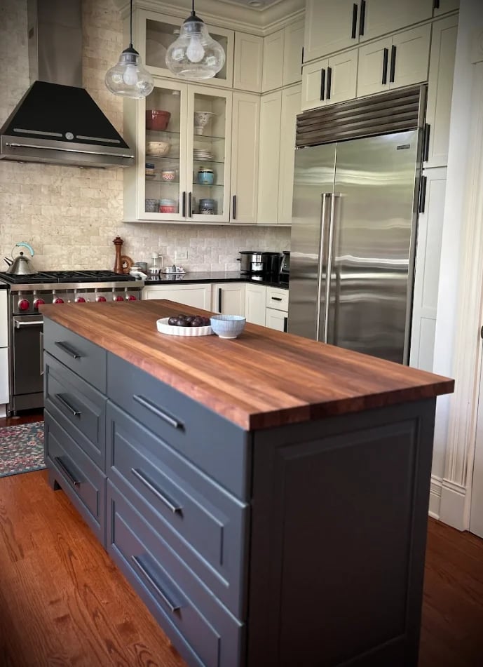 Modern kitchen with dark blue island featuring wood countertop, white cabinetry, stainless steel appliances, and pendant lights