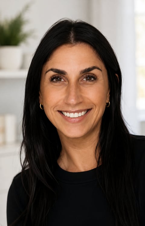 Professional headshot of a woman with long black hair, smiling at the camera, wearing a black top in a bright office setting