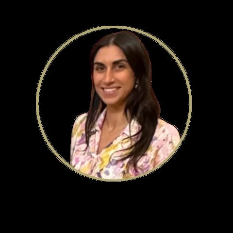 Woman with long dark hair smiling at camera, wearing a colorful floral and yellow patterned blouse in circular frame