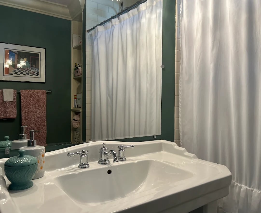Modern bathroom with white pedestal sink, chrome faucet, dark green walls, and white shower curtain