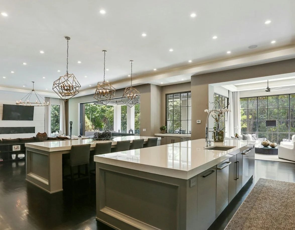 Modern open-concept kitchen with two-tier island, pendant lights, and large windows with green views